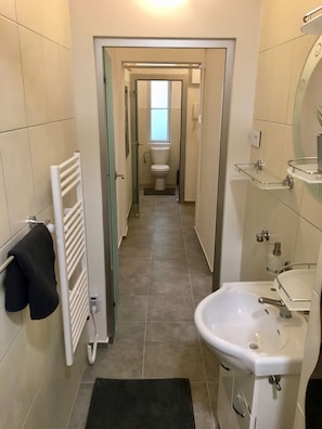 A narrow bathroom with a white sink, a glass shower enclosure, and a toilet visible down the hall. - Hybernska (Prague)