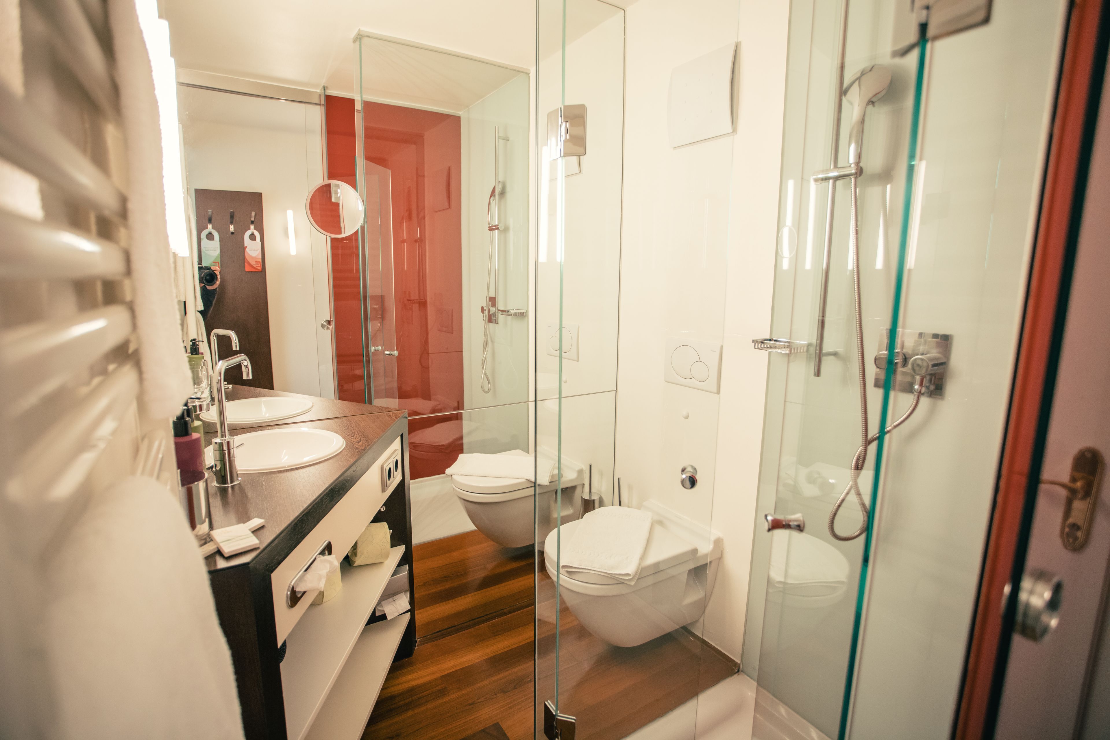 Un baño moderno con ducha envuelta en vidrio, tocador de madera y un inodoro independiente.