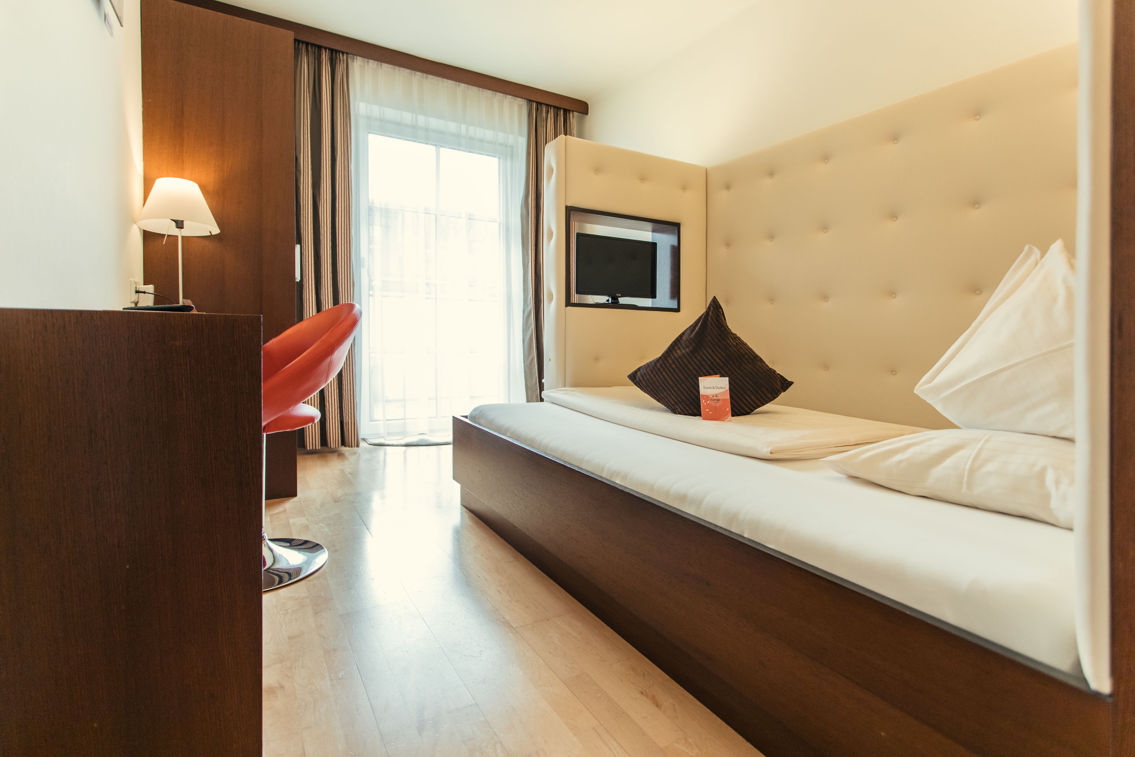 Habitación de hotel con cama, televisor, escritorio y una silla roja.