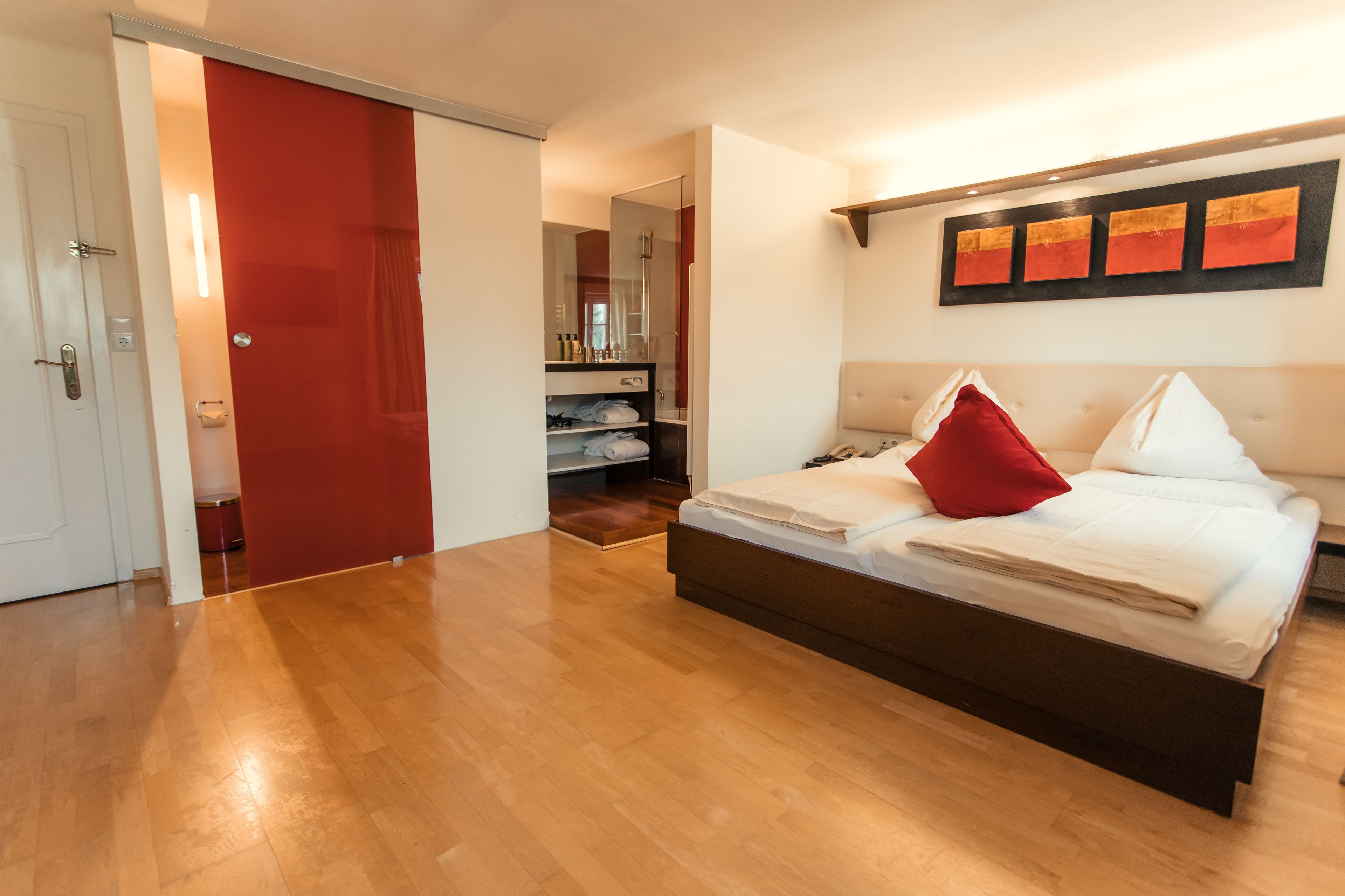 A bedroom with a large bed, a red door, and a hallway leading to a bathroom.