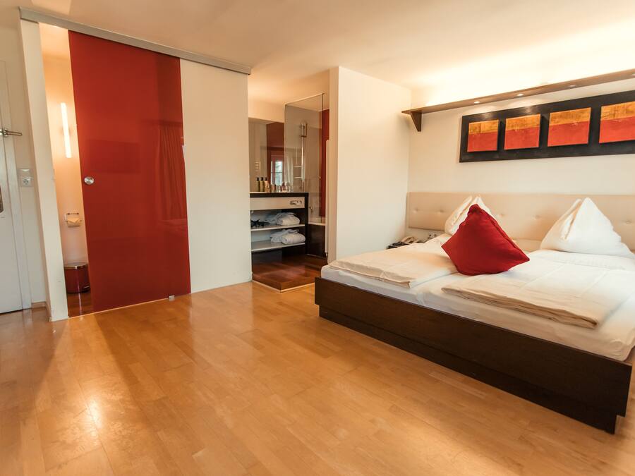 Un dormitorio con una cama grande, una puerta roja y un pasillo que da a un baño.