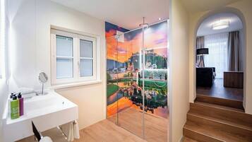 Een moderne badkamer met een glazen douchedeur, een wit aanrecht met een spiegel en uitzicht op een stadsbeeld door het glas.