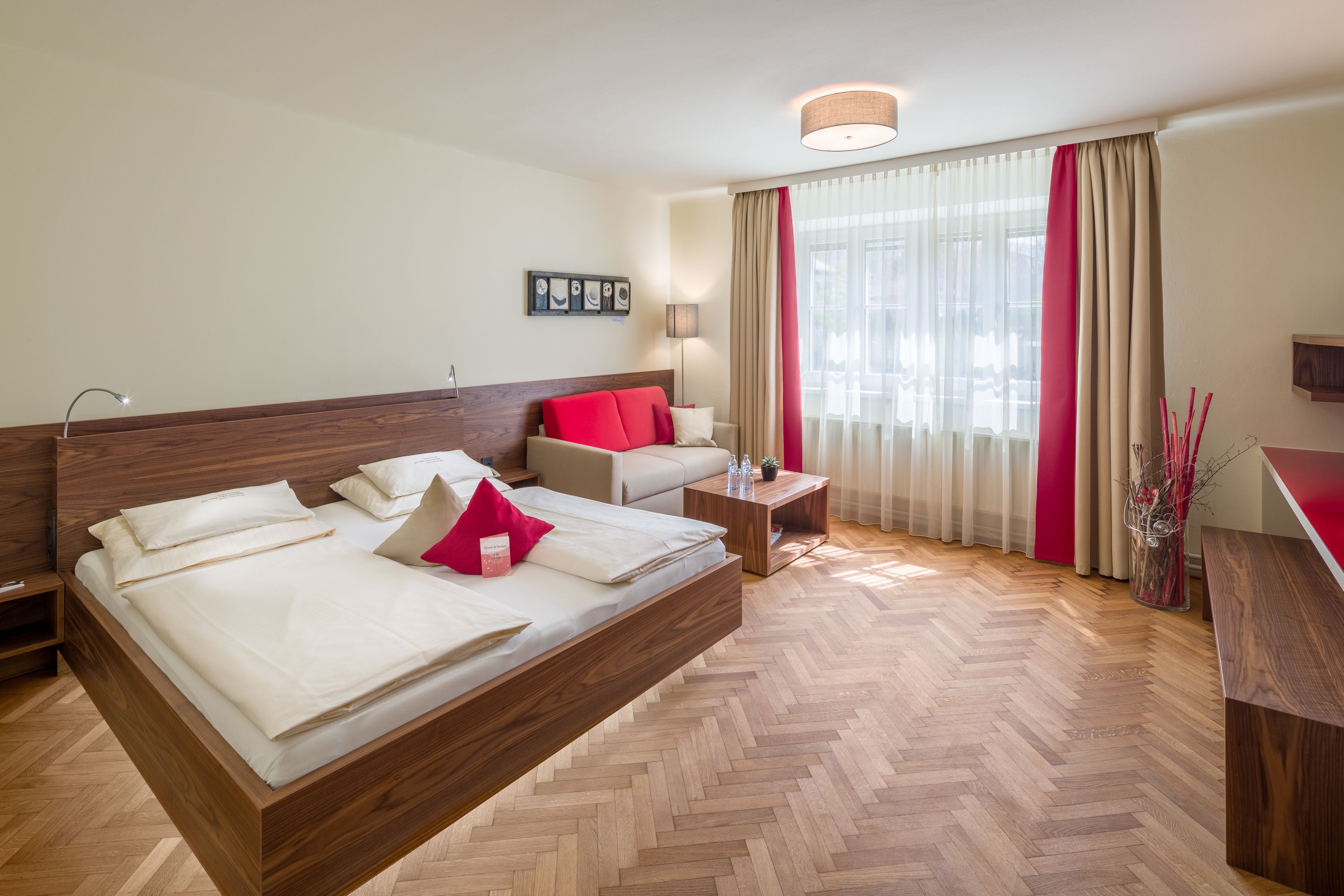 A modern hotel room with a large bed, a sofa, a small table, and a desk.