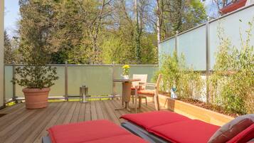 A wooden deck with two red beds, a small table with a chair, and a potted plant.