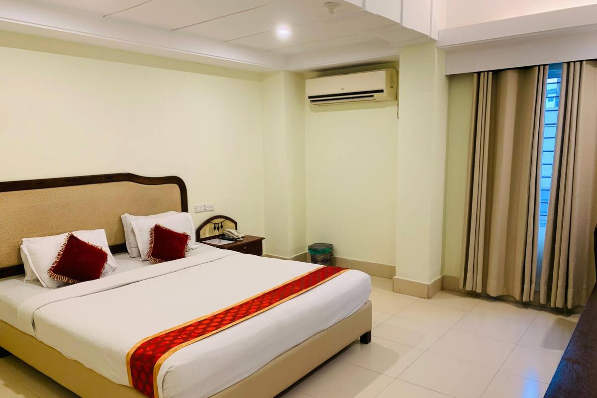 Quarto de hotel com cama, mesa de cabeceira, aparelho de ar condicionado e janela com cortinas.