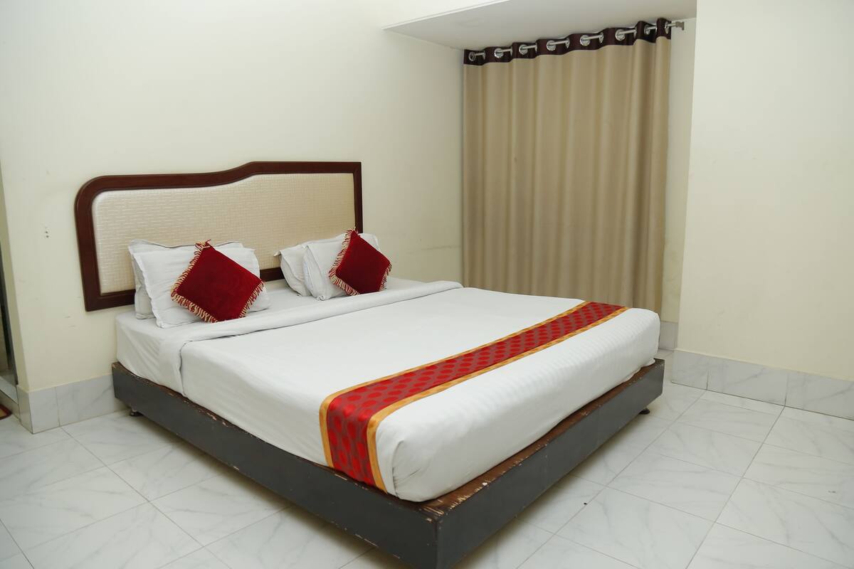 Cama bem arrumada com cabeceira, roupa de cama branca e manta com padrão vermelho e amarelo.