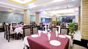 A restaurant with tables set for dining, featuring a central column and potted plants. - Panshi Inn (Sylhet)