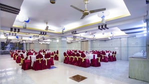 A banquet hall with rows of round tables, each with a white tablecloth and red chairs with gold sashes. - Panshi Inn (Sylhet)