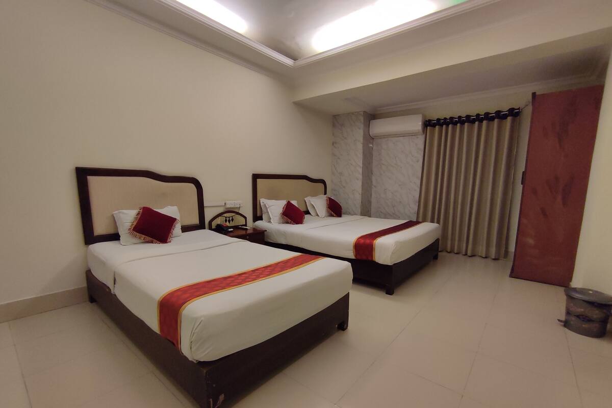 Quarto de hotel com duas camas, parede de mármore e janela com cortinas.