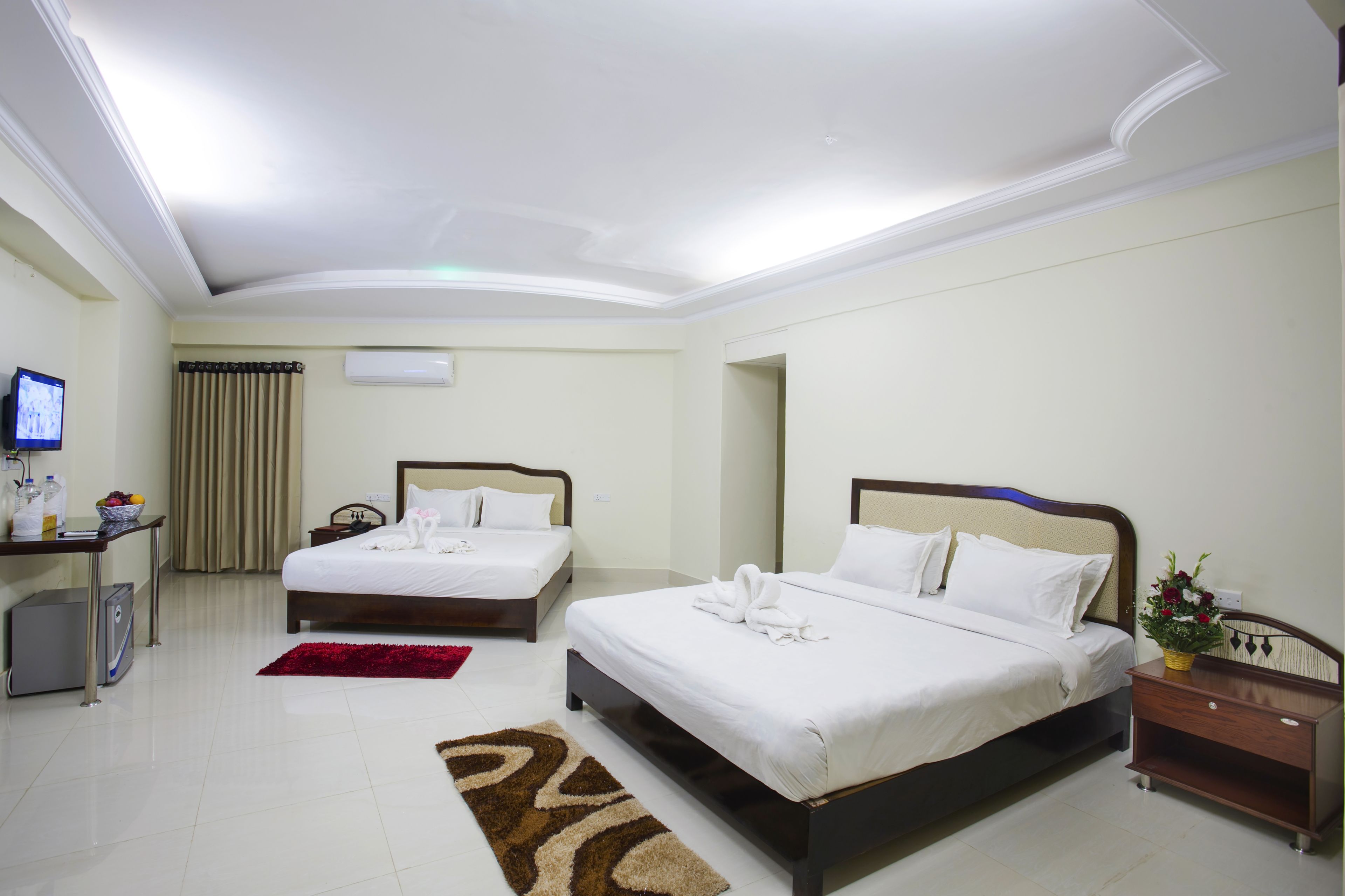 A hotel room with two beds, a desk, a TV, and a red rug.
