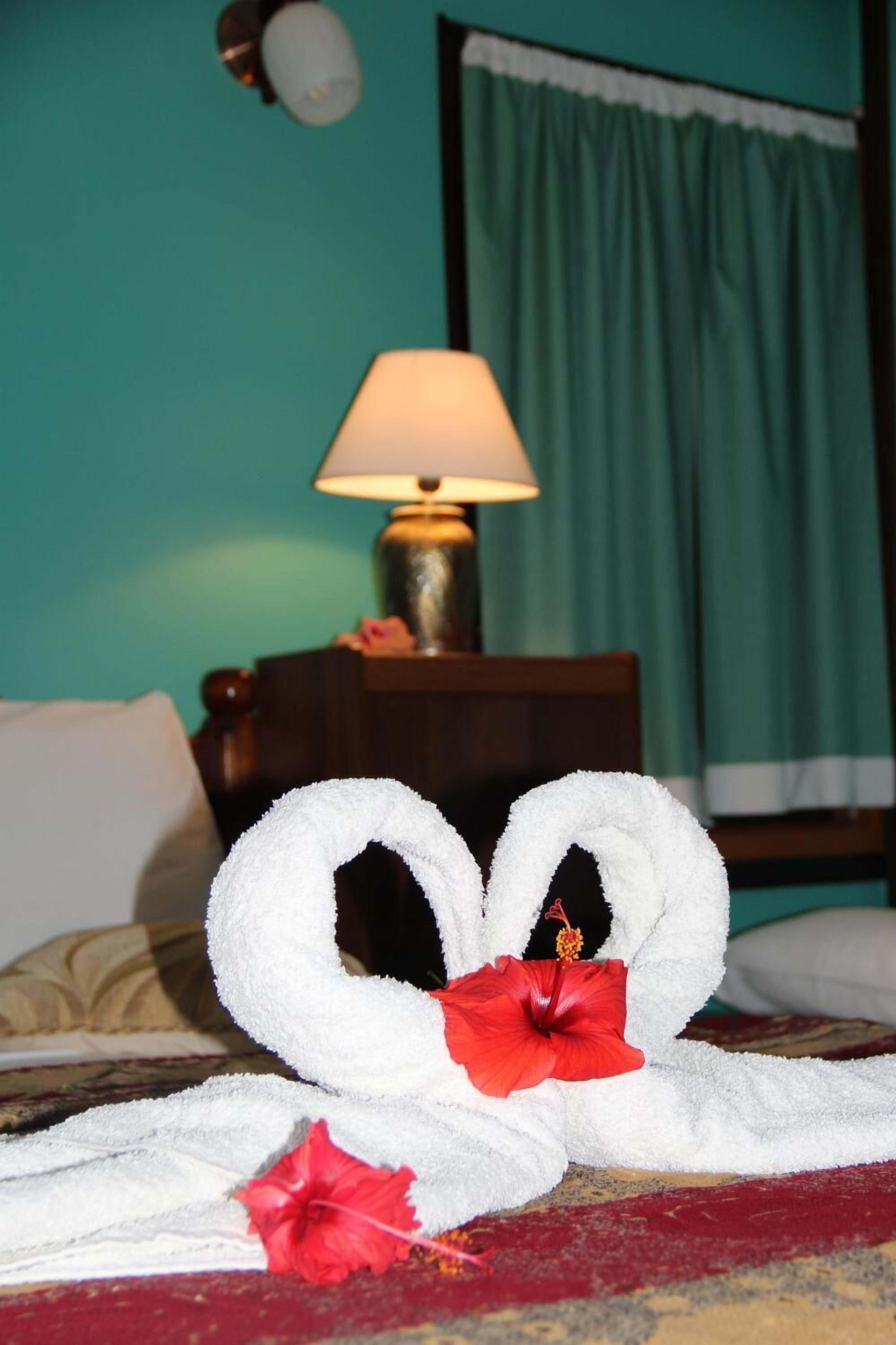 Una cama con una toalla blanca y una flor de hibisco rojo sobre ella.