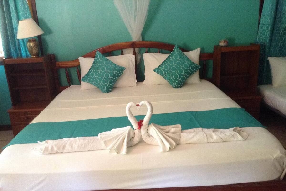 A bed with a swan towel arrangement, teal and white bedding, and matching pillows.