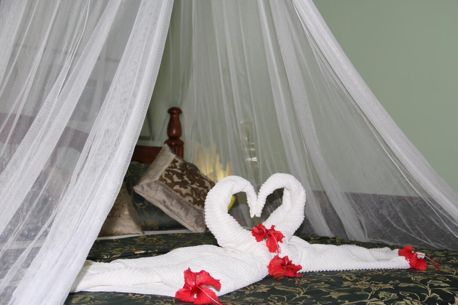 A bed with a canopy, a heart-shaped towel, and red flowers.