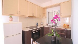 A modern kitchen with light wooden cabinets, a black countertop, a built-in oven, and a small potted orchid on the table. - AR Apartments by Saranda Hotel (Sarandë)
