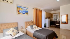 A hotel room with two beds, a kitchenette, and a painting on the wall. - AR Apartments by Saranda Hotel (Sarandë)