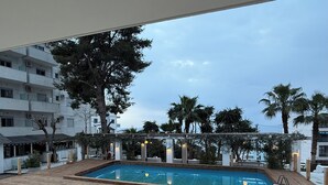 An outdoor swimming pool with a wooden deck, surrounded by palm trees and a building with balconies. - AR Apartments by Saranda Hotel (Sarandë)