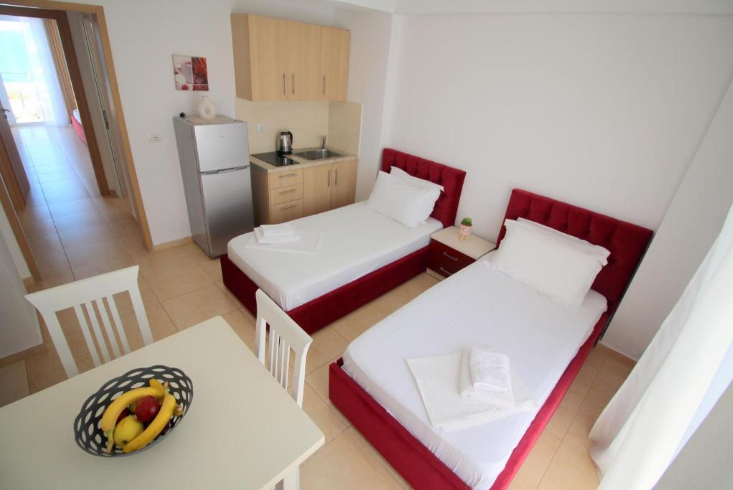 A compact hotel room with two beds, a small kitchenette, a dining area, and a view of the outside.