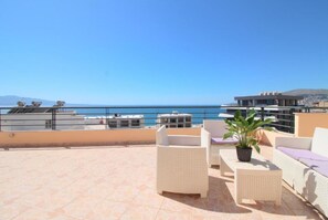 A rooftop terrace with wicker furniture, a potted plant, and a view of the sea.