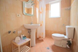 A bathroom with a sink, toilet, and a small table with toiletries.