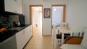 A compact kitchen with a black marble countertop, a sink, and a dishwasher. There is a dining area with a white table and chairs, and a small potted plant on the table. - AR Apartments by Saranda Hotel (Sarandë)
