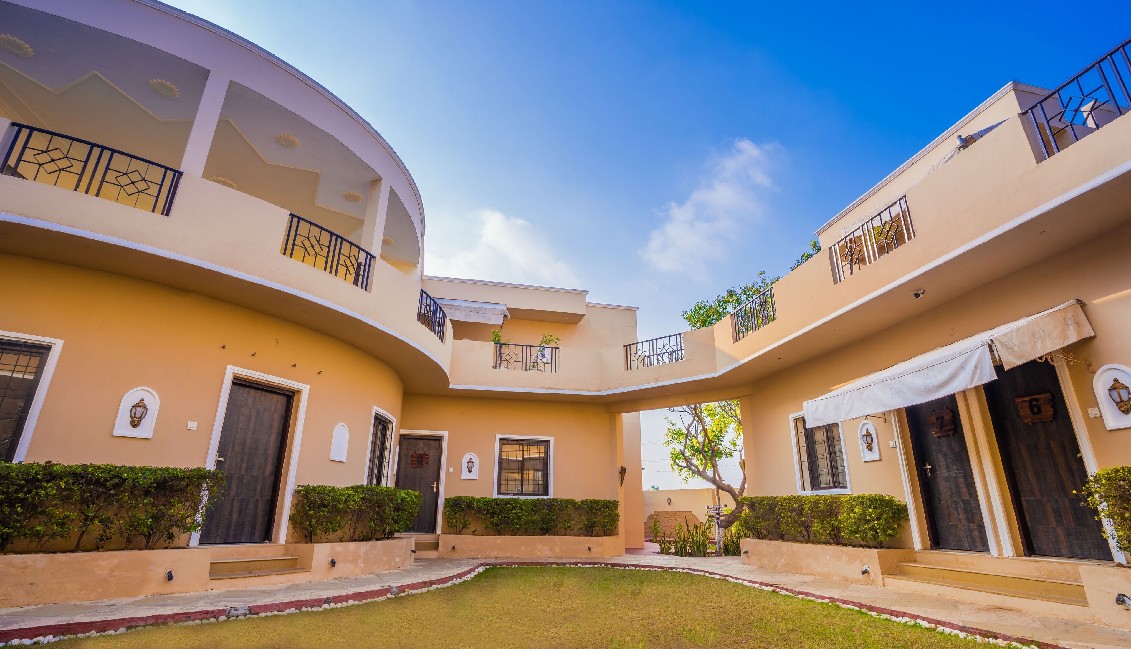A multi-story building with a curved facade, balconies with metal railings, and a central courtyard with a lawn.