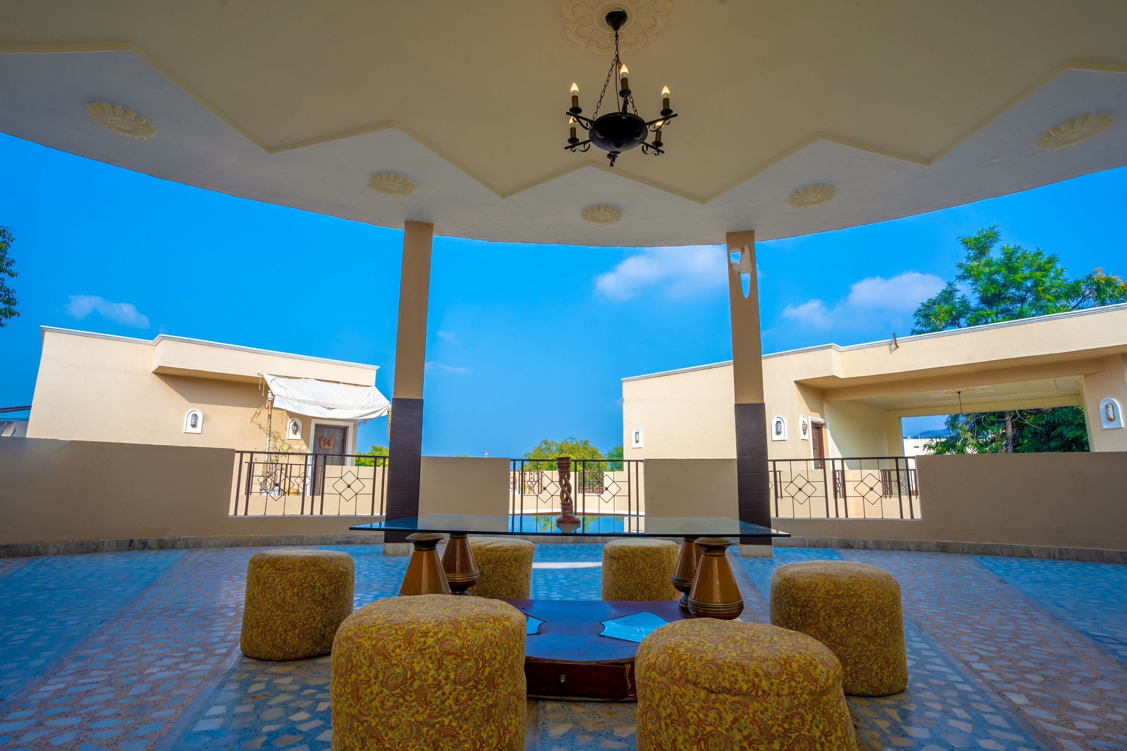 A covered outdoor seating area with a table and chairs, a chandelier, and a view of buildings in the background.