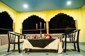 A dining area with a table set for two, featuring a candelabra with candles, a vase with flowers, and a decorative table runner. - Shani Vilas - Ranthambore (Sawai Madhopur)