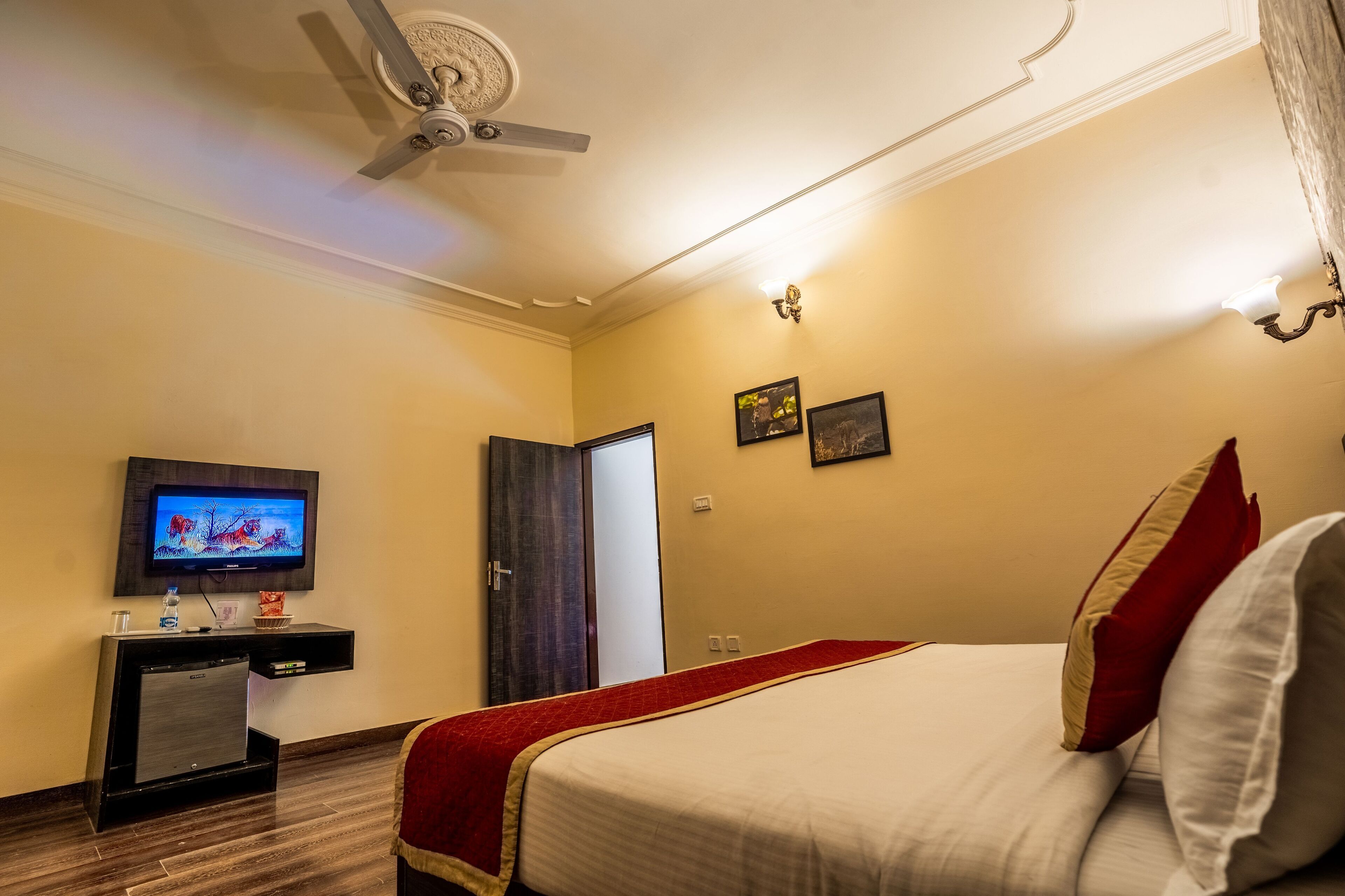 A hotel room with a bed, a television on a stand, a ceiling fan, and a door.