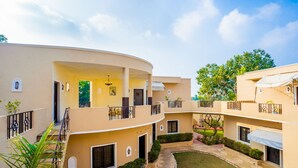 A multi-story building with a curved facade, balconies, and a central courtyard with a lawn and stone pathway. - Shani Vilas - Ranthambore (Sawai Madhopur)