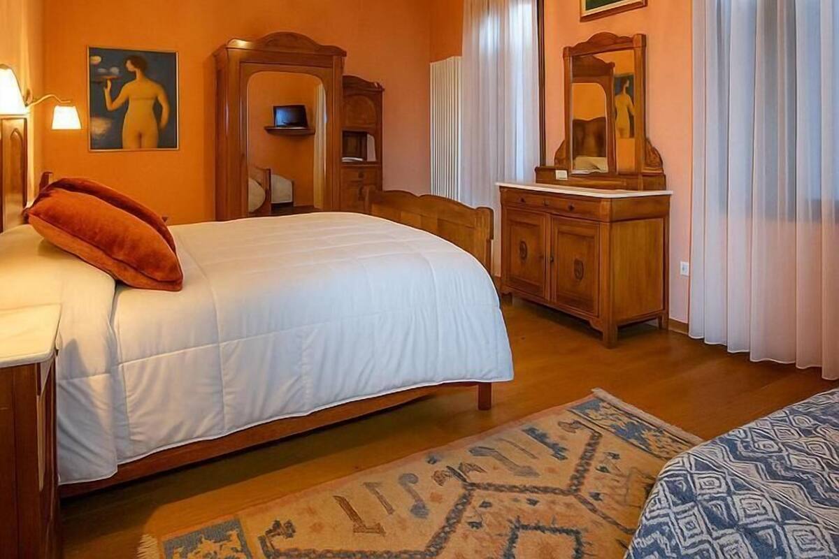Hotellihuone, jossa on sänky, puinen lipasto, peili ja kattokruunu.