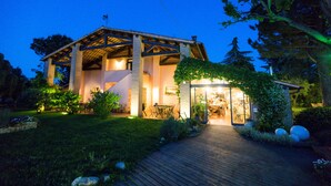 A house with a wooden deck, a covered patio, and a well-lit interior. - Trere Agriturismo (Faenza)