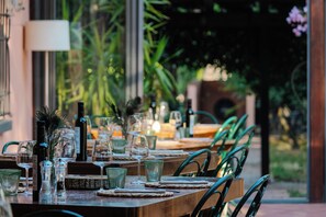 Una mesa de comedor preparada con copas de vino, copas de agua y cubiertos, rodeada de sillas.