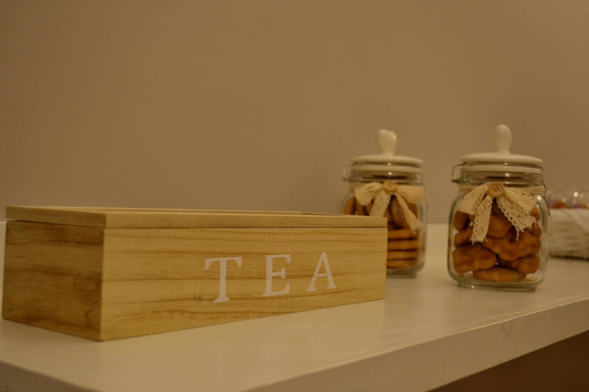 Een houten bordje met de tekst 'TEA' op een plank, vergezeld van twee glazen potten met deksels, waarschijnlijk gevuld met thee of koekjes.