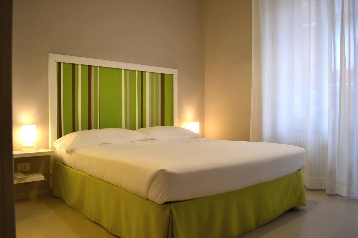 A neatly made bed with a green and white striped headboard, a white bedspread, and a green skirt. There are two bedside lamps on either side of the bed.
