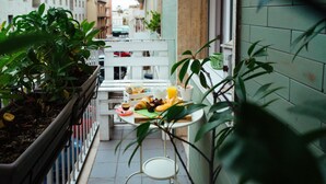 Un petit balcon extérieur avec une table préparée pour le petit-déjeuner, comprenant des croissants, un panier de fruits et un verre de jus d’orange.