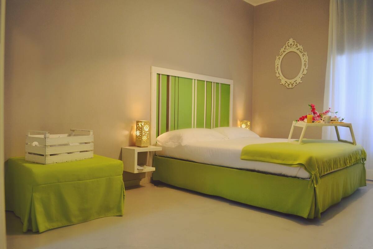 A bedroom with a bed, a nightstand, a bedside table, and a mirror on the wall.