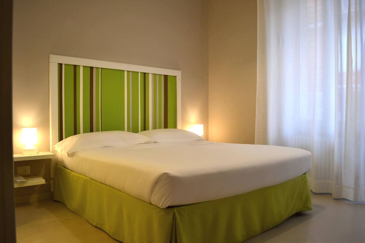 A neatly made bed with a green skirt, a white headboard, and two bedside lamps.