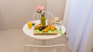 Une table blanche dressée pour le petit-déjeuner, avec des croissants, un verre de jus d’orange, un vase avec une fleur et une assiette de viennoiseries.