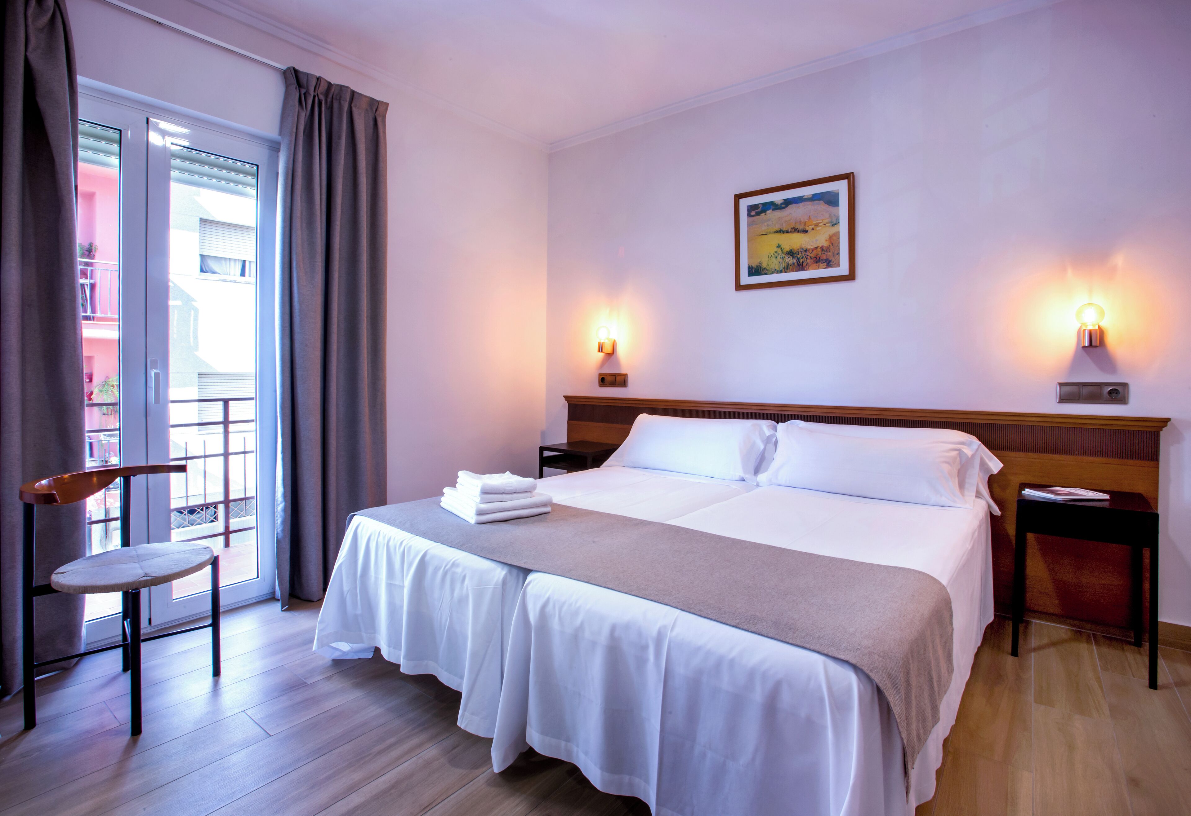 Una habitación de hotel con una cama, una silla, una mesita de noche y un cuadro en la pared.