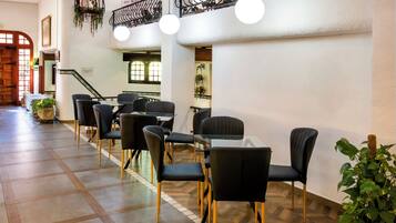 A hotel lobby with a long reception desk, black chairs, a glass table, and a staircase with a wrought iron railing.