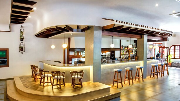 A bar area with a curved counter, wooden stools, and a modern interior design. - Hotel Ramis (Ondara)