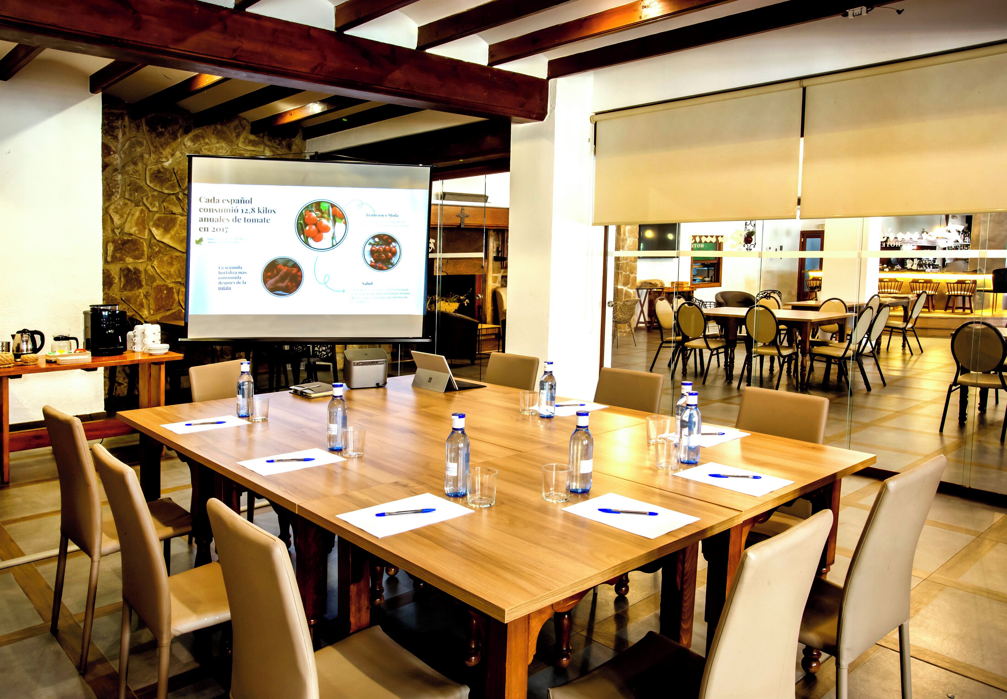 Una sala de conferencias con una mesa grande, sillas, una pantalla de proyector y una estación de café.