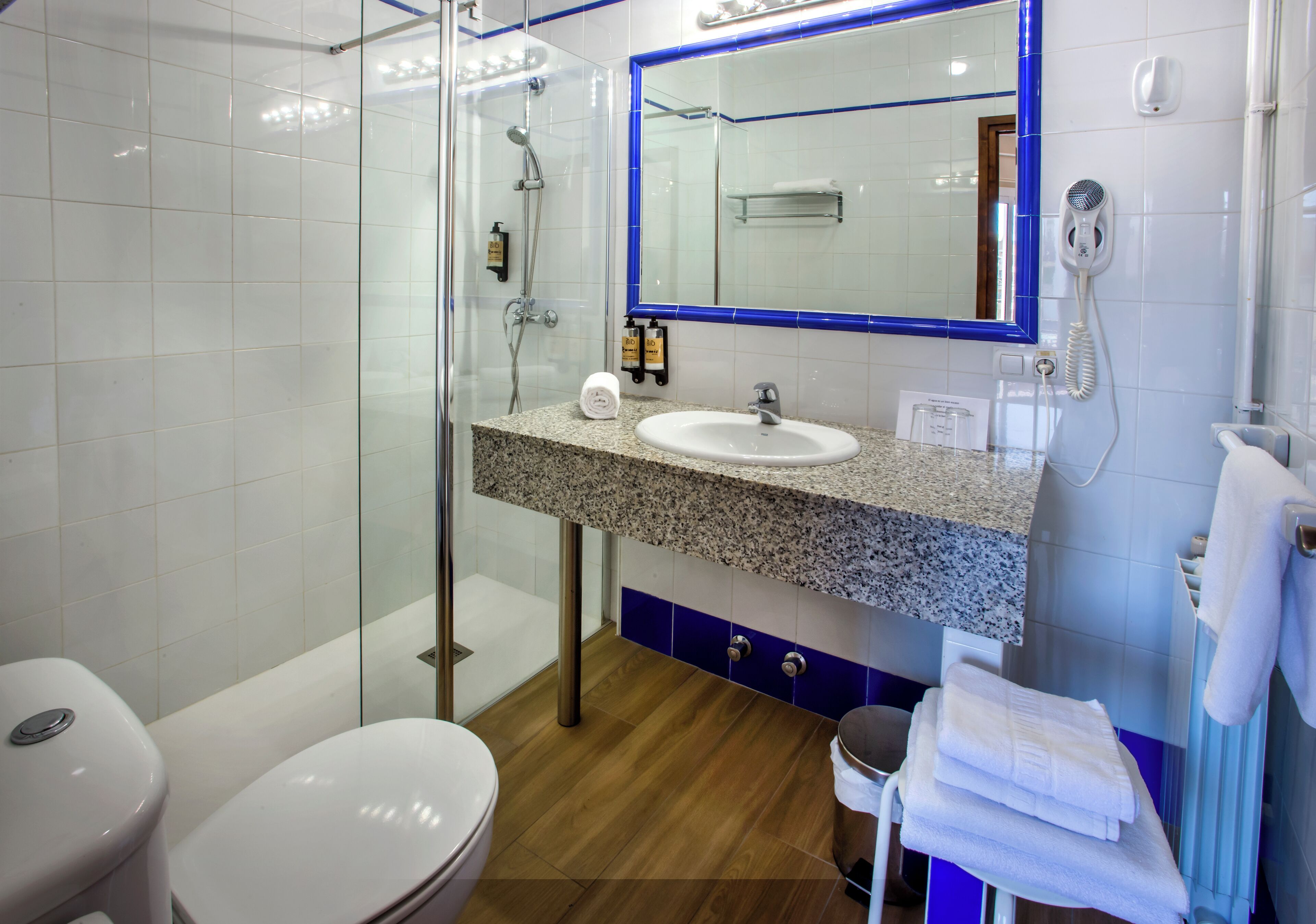 Un baño moderno con cabina de ducha de vidrio, lavabo con encimera de granito y espejo con marco azul.