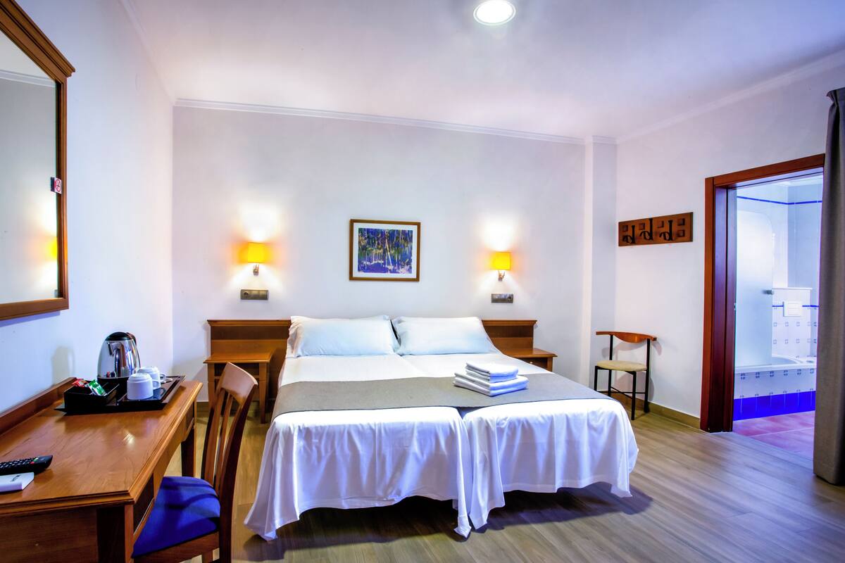 Habitación de hotel con cama, dos mesitas de noche, un escritorio, una silla y un baño visible a través de una puerta abierta.