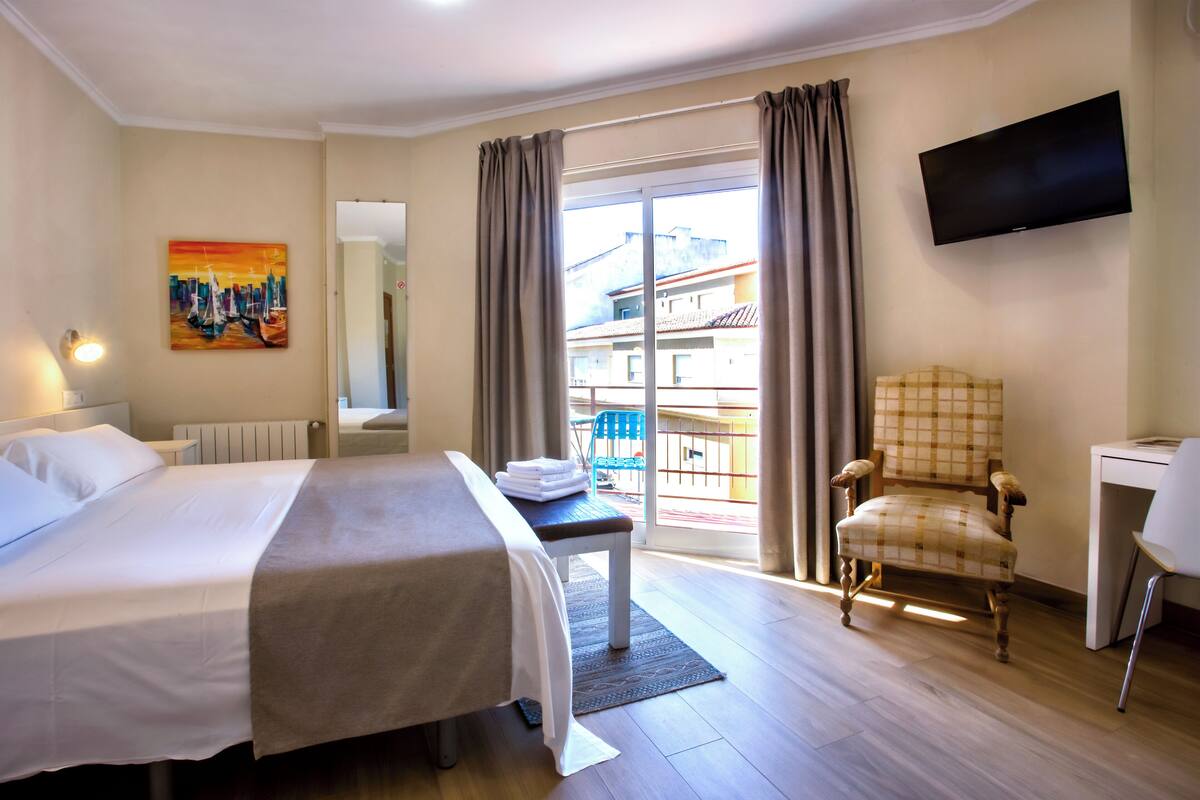 Habitación de hotel con cama, una silla, un escritorio, un televisor y vistas al exterior.