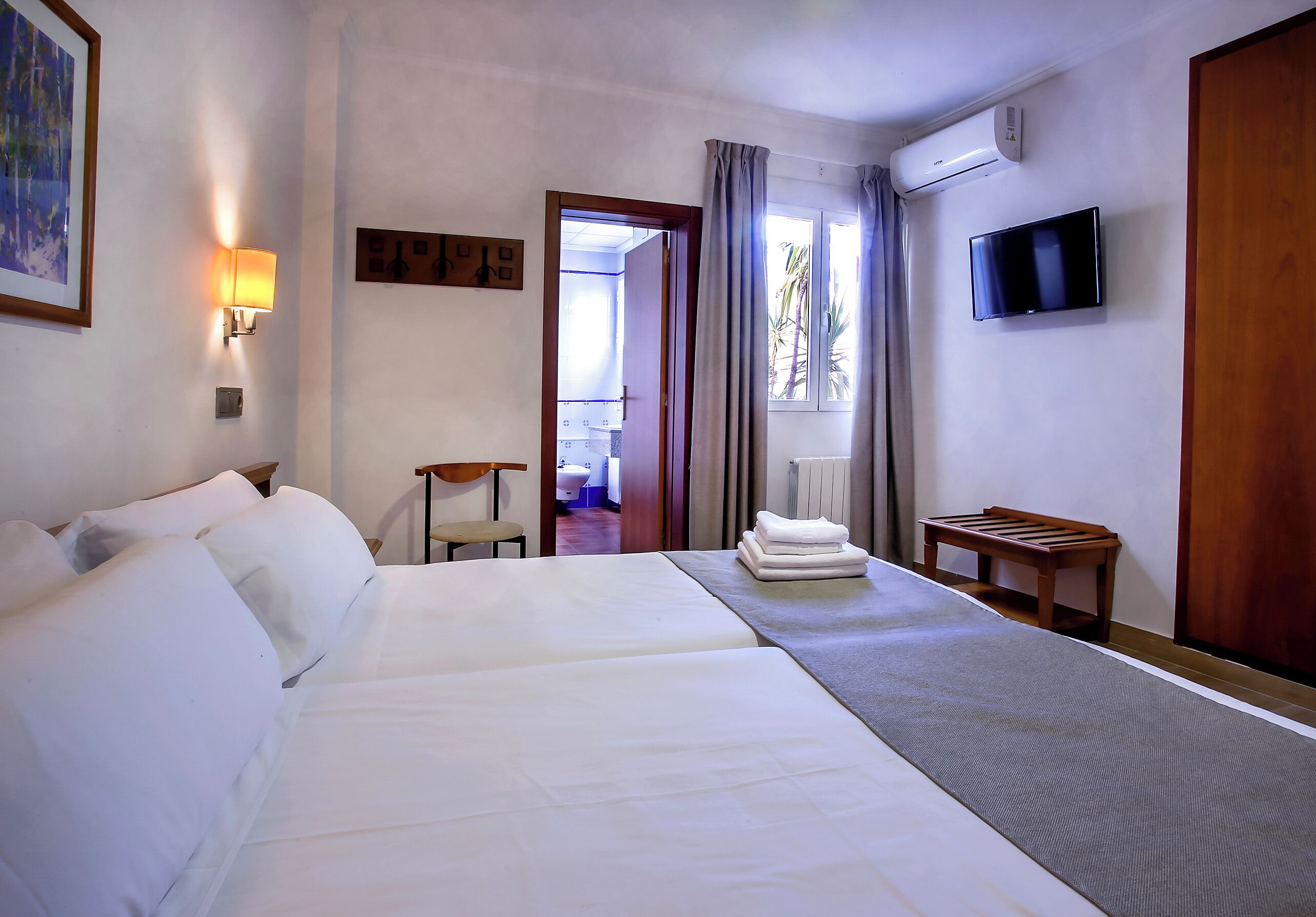 A hotel room with two beds, a television, a desk, and a window with curtains.