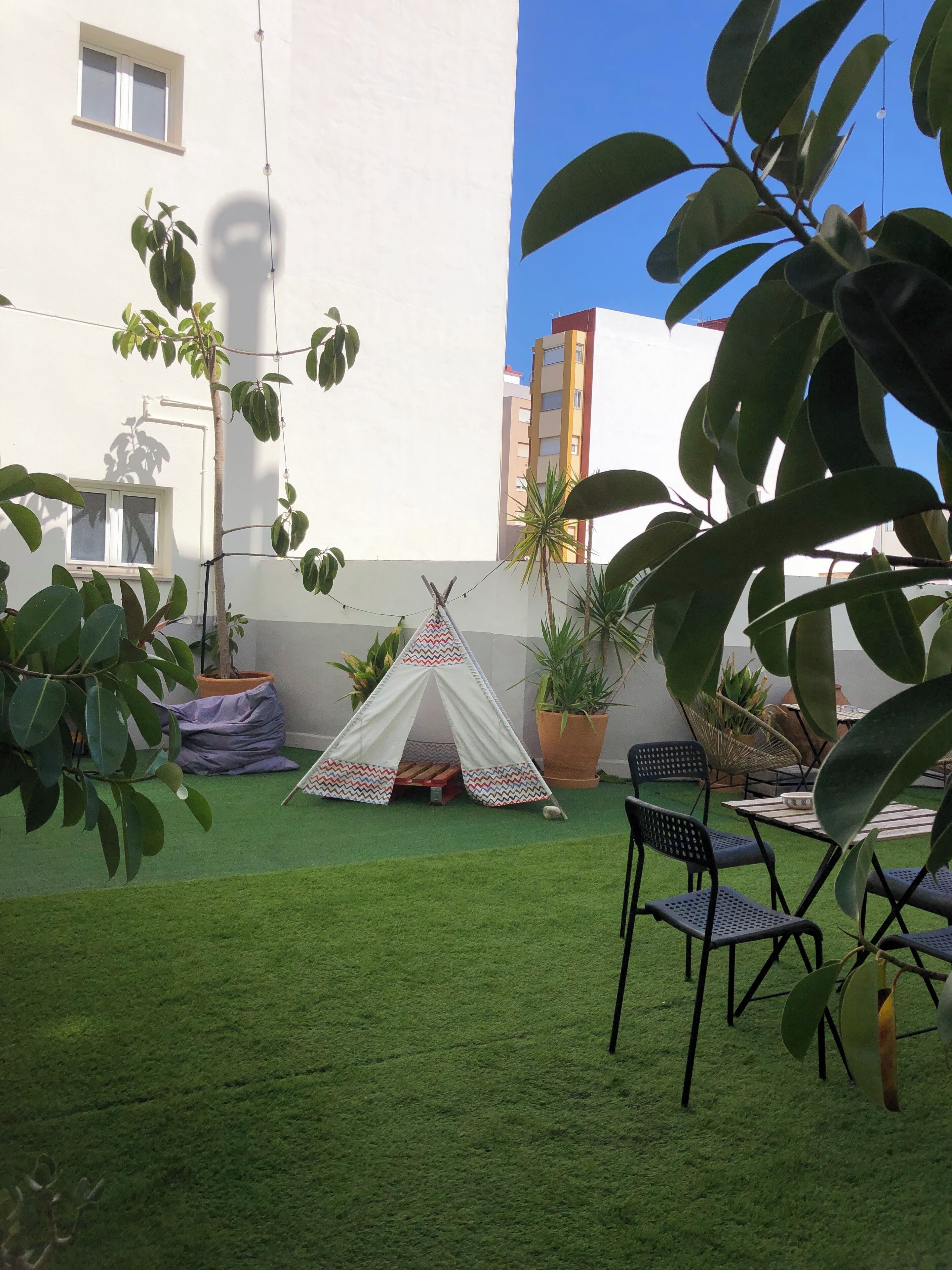 Een binnenplaats met kunstgras, een tipi, potplanten en tuinmeubilair.