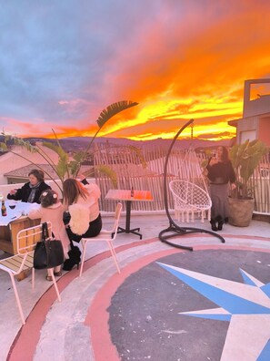 Un espacio al aire libre con mesas y sillas, vista al atardecer y un diseño decorativo en el suelo.