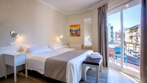 A hotel room with a bed, bedside tables, a bench, a large window with a view of buildings, and a painting on the wall. - Hotel Ramis (Ondara)