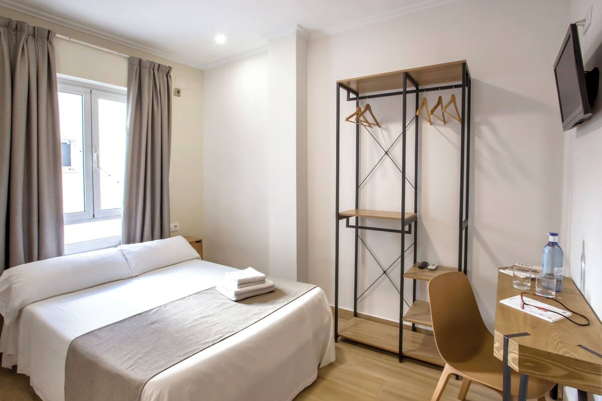 Habitación de hotel con cama, escritorio, silla, armario y televisor.